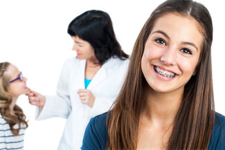 young girl with braces smiling, orthodontist in background with another female patient braces in Rockwall, TX