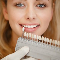 woman smiling as dentist holds up color samples of teeth for creating dental veneers Melrose, MA dentist