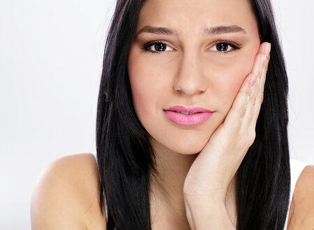 young dark haired woman holding hand against jaw in pain, TMJ treatment Santa Rosa Beach, FL