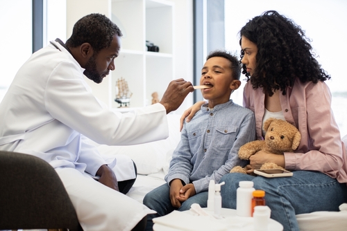 Pediatrician examining a sick child's throat for signs of infection.