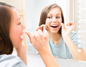 teen girl flossing teeth looking in mirror, orthodontics Sioux Falls, SD orthodontist