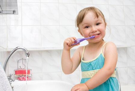 blond toddler girl standing at bathroom sink brushing teeth, pediatric dentistry Decatur, IL children's dentistry 