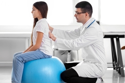 Doctor checking the back of young girl for physical exam