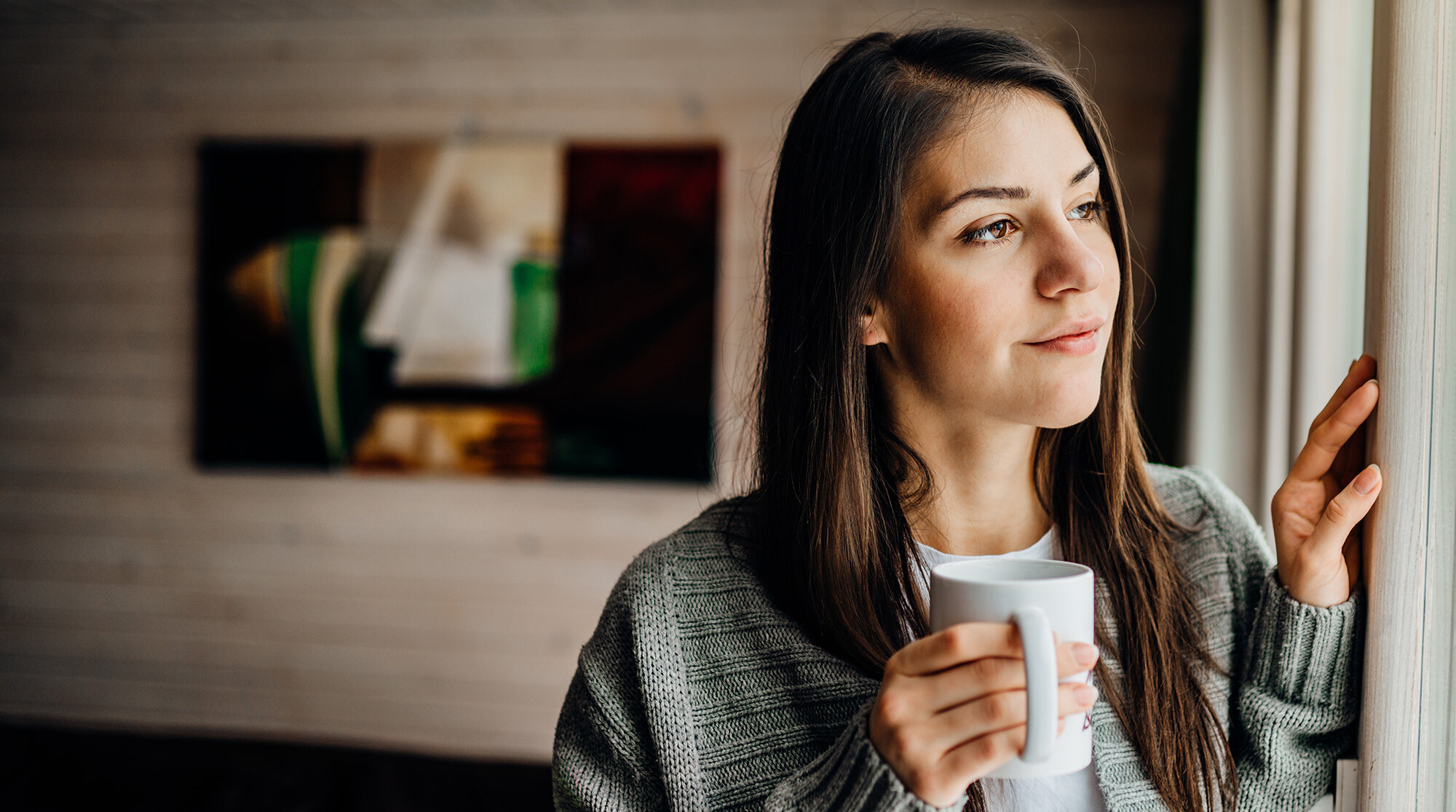 Woman holding coffee cup looking out window